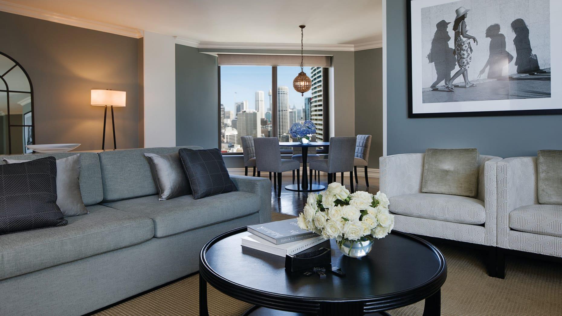 Four Seasons Hotel Sydney Exterior photo The photo shows a modern living room with a stylish and contemporary design. On one side, there is a gray sofa adorned with decorative pillows. A round black coffee table sits in front of the sofa, featuring a vase with white flowers and some books. 