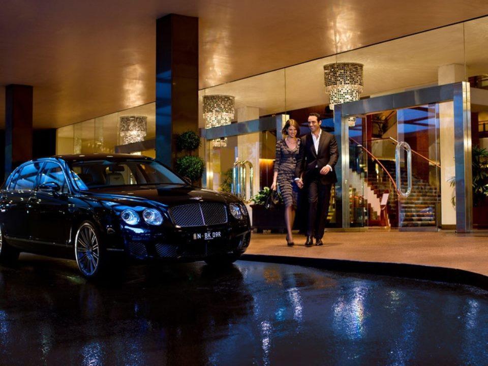 Four Seasons Hotel Sydney Exterior photo The photo depicts a luxurious scene outside a hotel. A sleek black car is parked nearby, and a well-dressed couple is walking hand in hand towards the entrance of the hotel. The surroundings are elegant, with a modern architectural style, and the ent